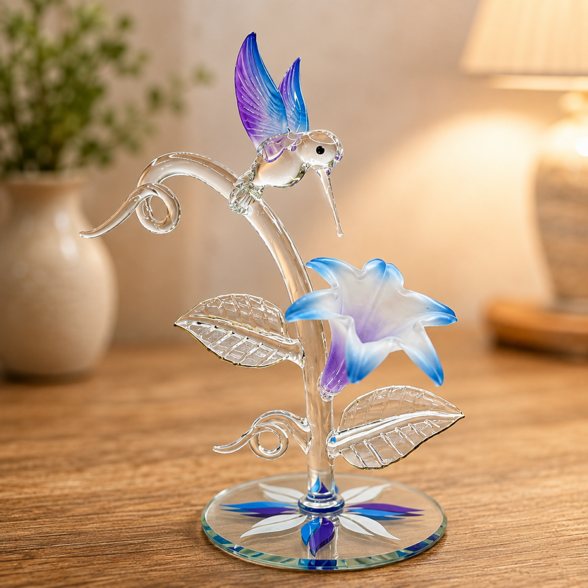 Handcrafted clear glass hummingbird sculpture hovering over a blue and purple lily on a vine with crystal and 22Kt gold accents