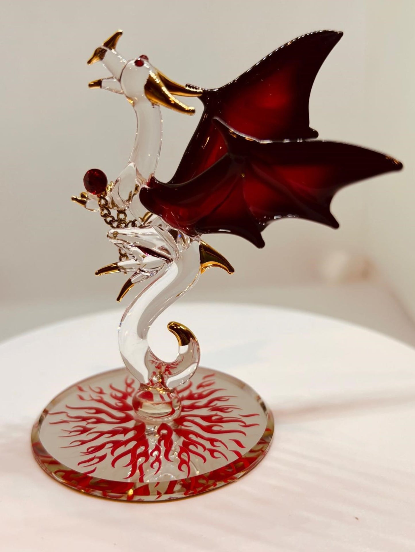 Handcrafted glass dragon figurine with red wings holding a crystal gem on a beveled mirror base