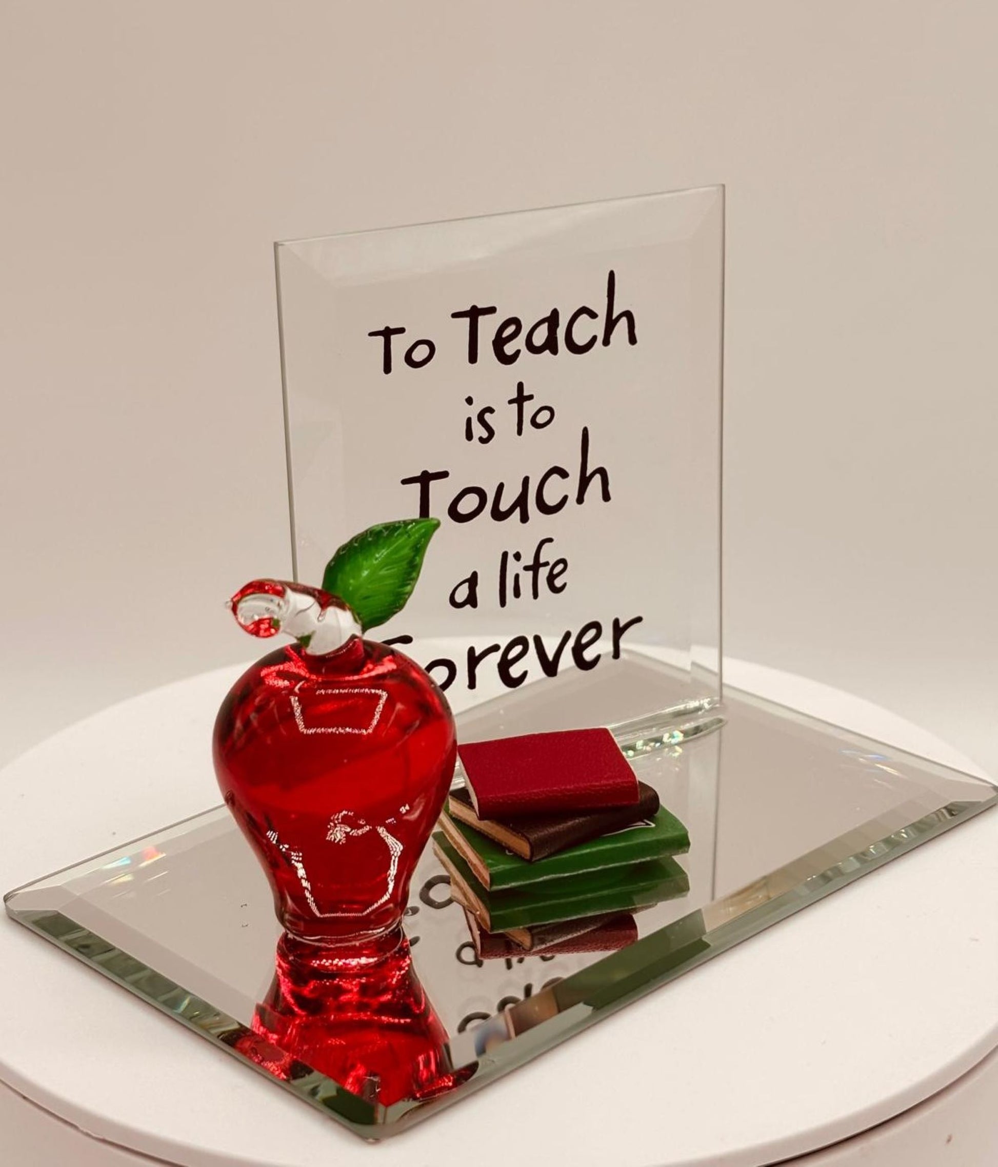 Handcrafted glass apple with books on mirrored base featuring “To Teach is to Touch a Life Forever” message