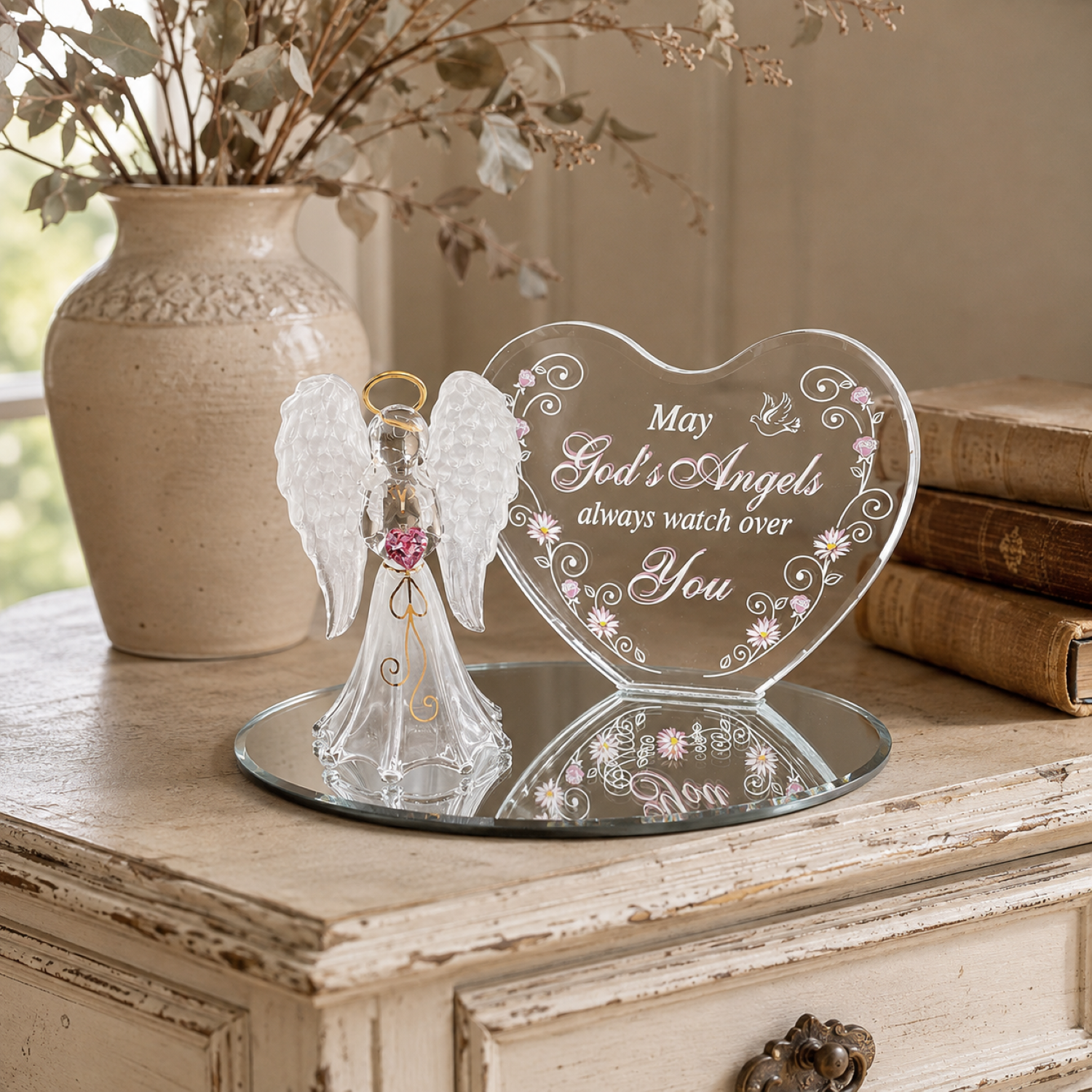 Handcrafted glass angel figurine with pink crystal heart beside a heart-shaped plaque reading “May God’s Angels always watch over You,” displayed on a mirrored glass base.