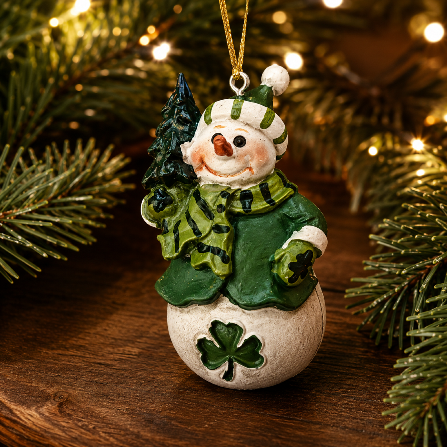 Resin snowman Christmas ornament wearing a green coat and scarf, holding a pine tree, with hanging cord.