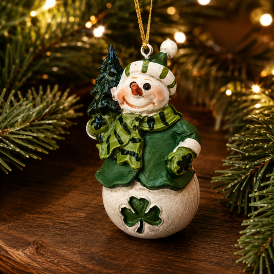 Resin snowman Christmas ornament wearing a green coat and scarf, holding a pine tree, with hanging cord.