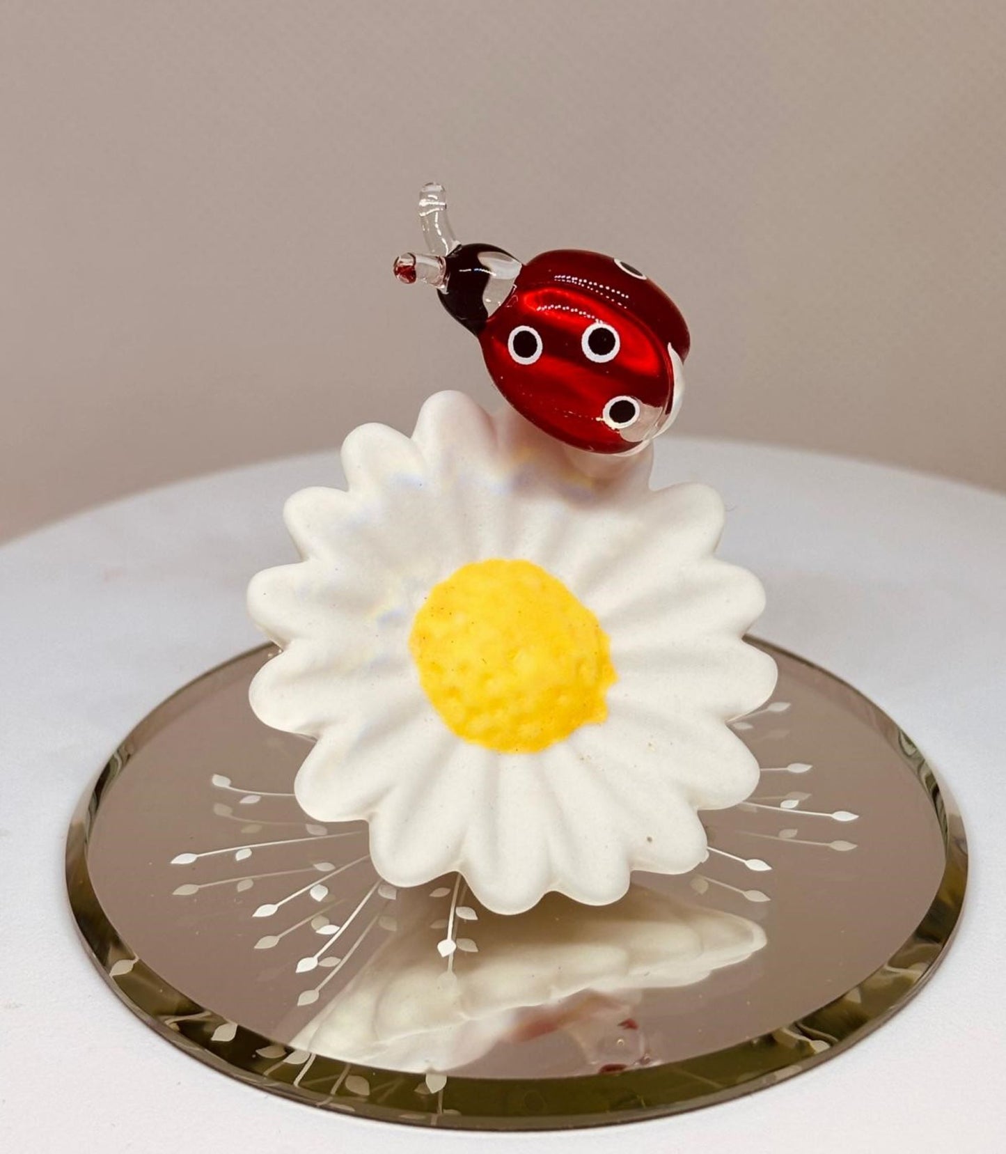 Handcrafted glass ladybug figurine on a daisy displayed on a beveled mirror base