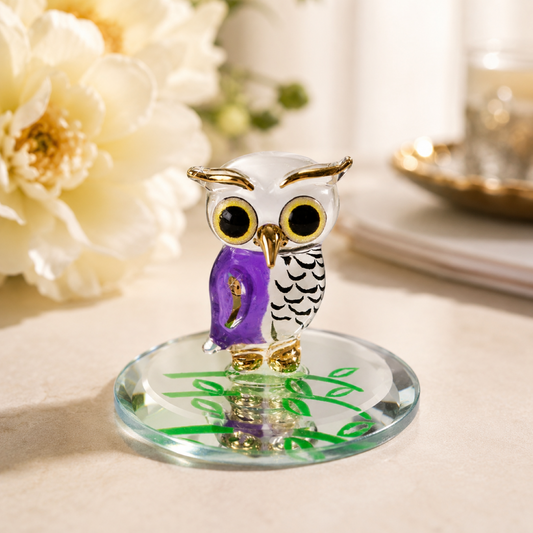 Handcrafted white and lavender glass owl figurine with Real 22Kt Gold accents displayed on a hand-beveled glass mirror with a green leaf design.