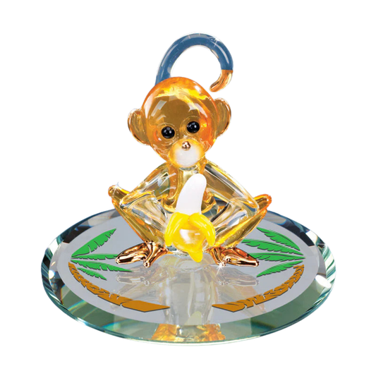 Glass monkey figurine holding banana on mirror base