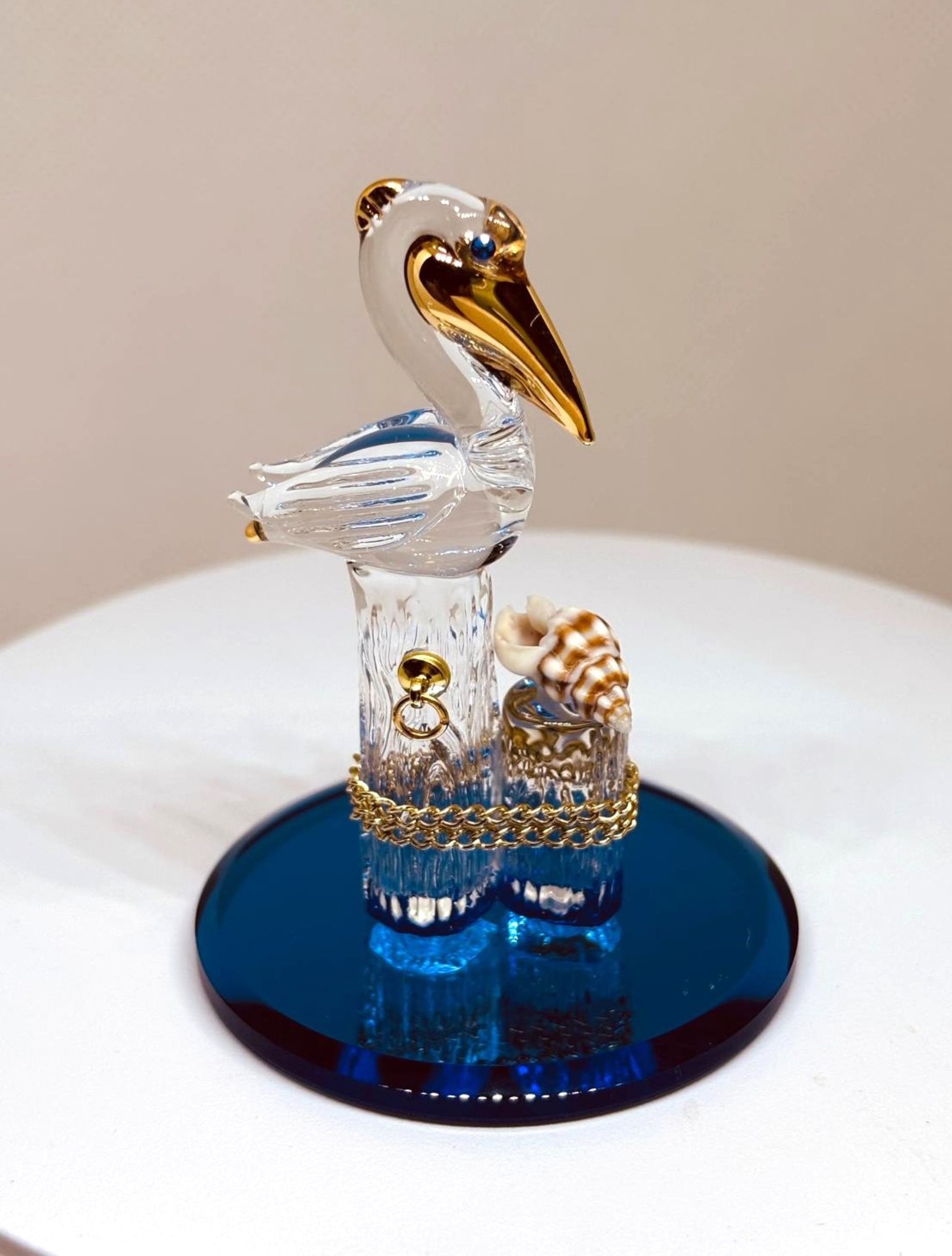 Handcrafted glass pelican perched on piling with shell and gold accents on blue base