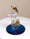 Handcrafted glass pelican perched on piling with shell and gold accents on blue base