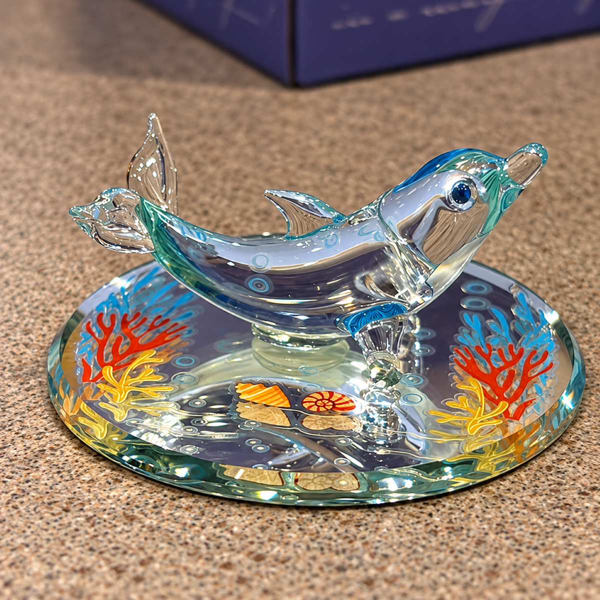 Handcrafted glass dolphin figurine with blue details on a decorative mirror featuring colorful coral reef designs