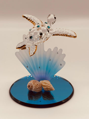 Handcrafted sea turtle with blue coral glass figurine accented with crystals and 22Kt gold on a blue mirror base. A peaceful coastal décor collectible for ocean lovers.