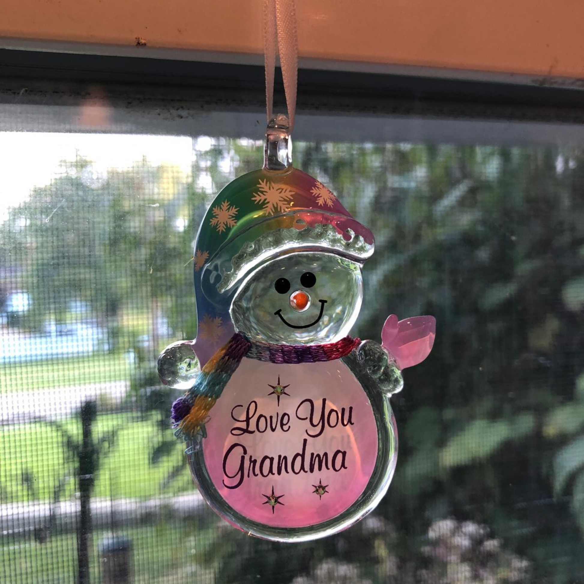 Handcrafted glass snowman ornament with pink “Love You Grandma” message hanging from ribbon.