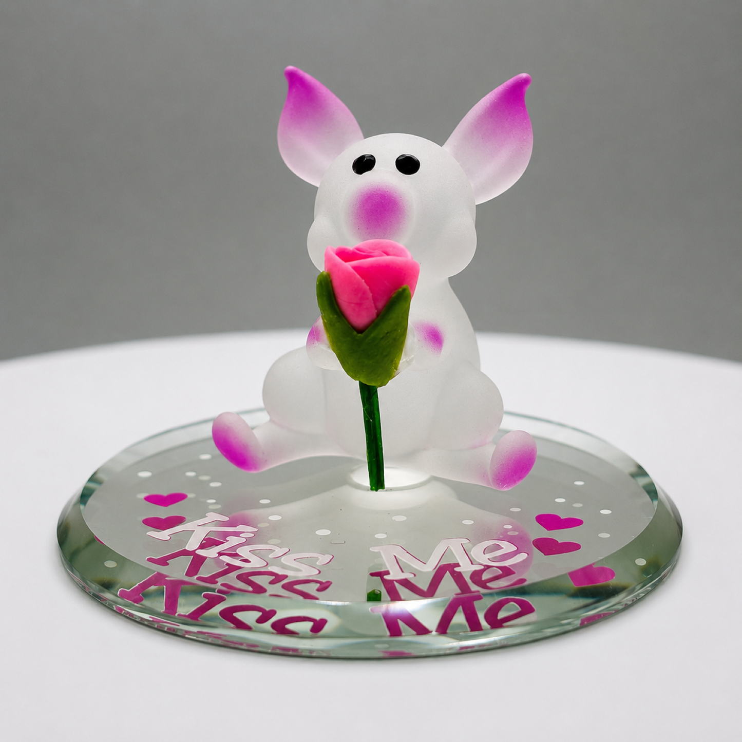 Handcrafted white and pink glass pig figurine holding a pink rose on a beveled glass mirror with the message "Kiss Me."