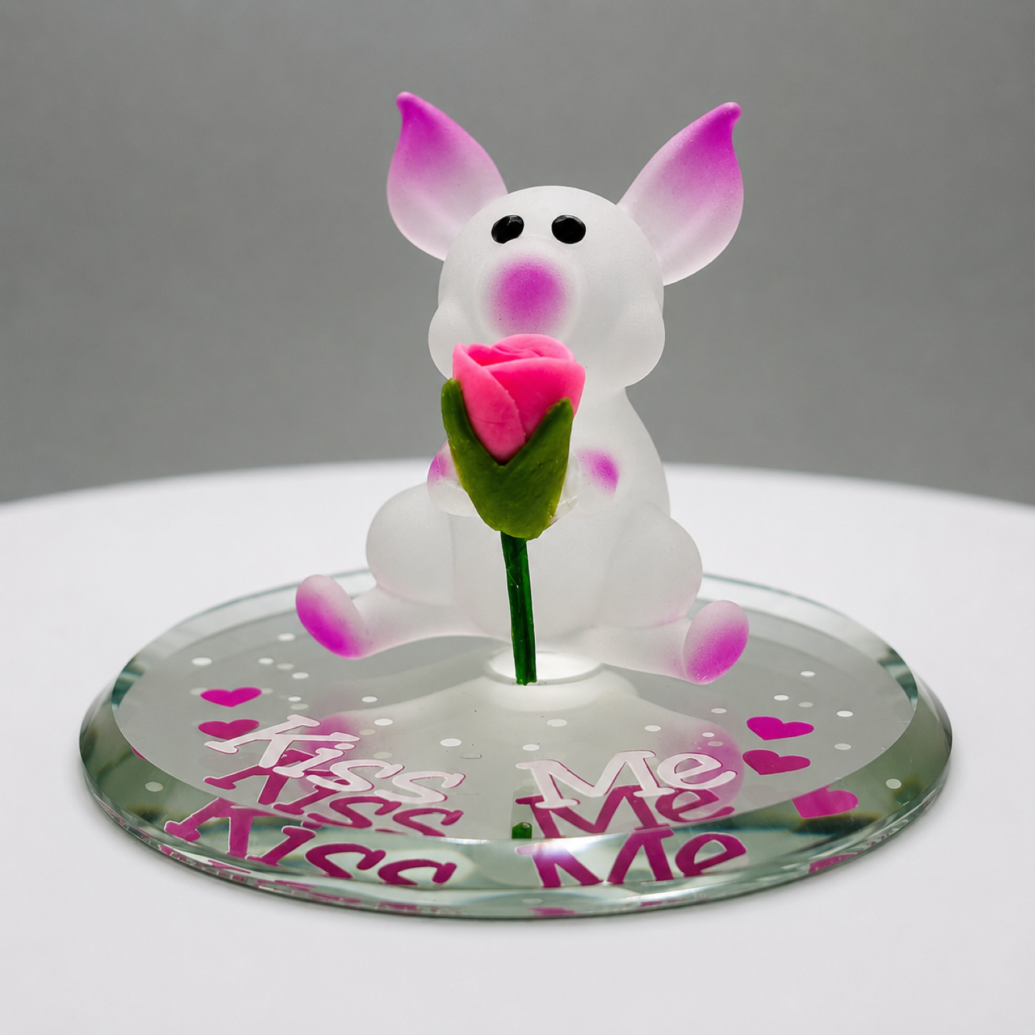 Handcrafted white and pink glass pig figurine holding a pink rose on a beveled glass mirror with the message "Kiss Me."